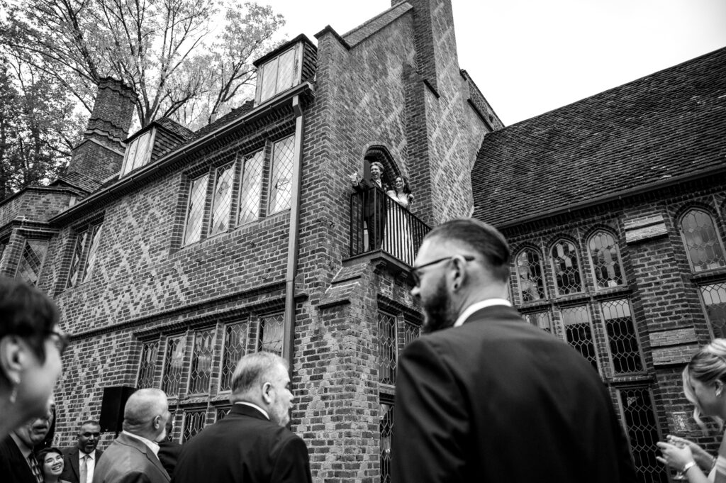 bride and groom looking out at guests from a balcony