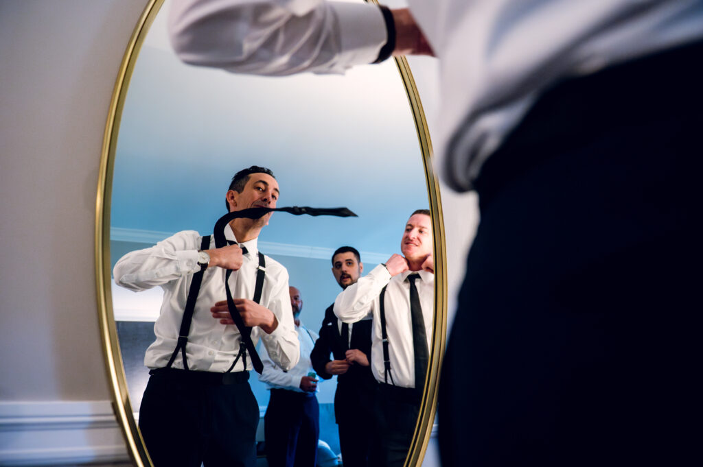 groom tying tie with groomsmen watching